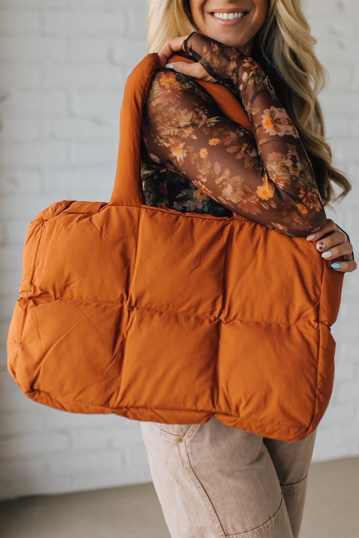 Person holding an orange puffer bag against a neutral background