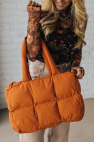 Person holding an orange puffer bag against a white brick wall.