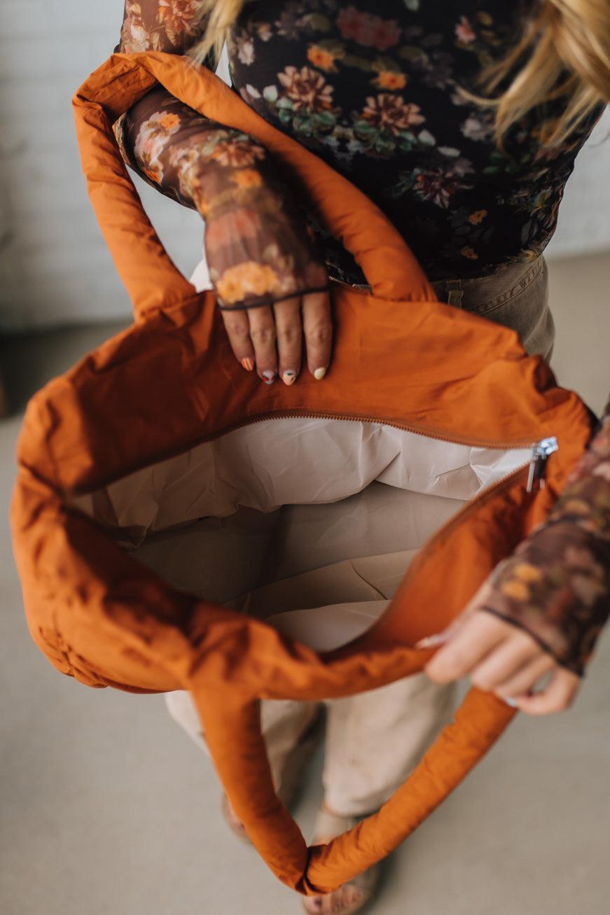 Person holding an orange bag with a floral-patterned sleeve.