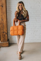 Woman holding an orange bag against a white brick wall.