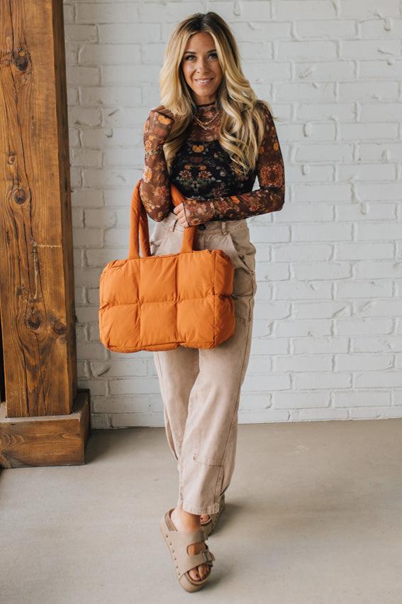 Woman holding an orange bag against a white brick wall.
