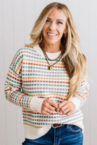 Blonde woman standing in brightly lit studio wearing a multi color sweater that has a relaxed, slightly cropped fit hits just right over high-waisted denim jeans.