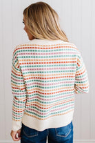 Blonde woman standing in brightly lit studio wearing a multi color sweater that has a relaxed, slightly cropped fit hits just right over high-waisted denim jeans.