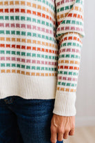 Blonde woman standing in brightly lit studio wearing a multi color sweater that has a relaxed, slightly cropped fit hits just right over high-waisted denim jeans.