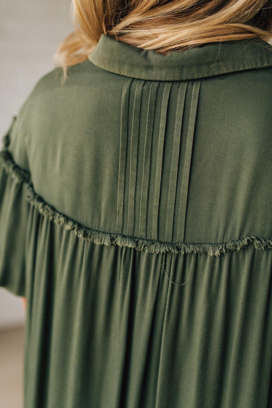 Green dress with pleated details and frayed hem on a neutral background