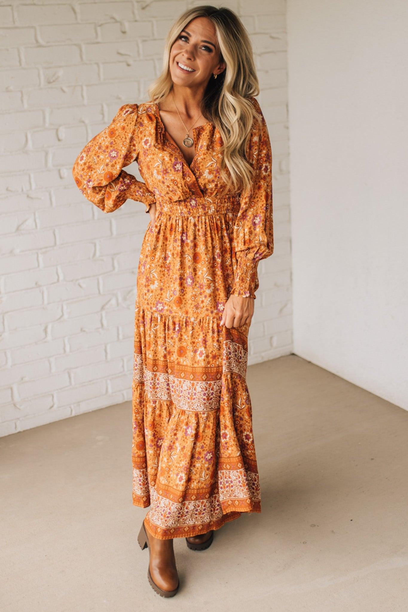 Woman wearing an orange floral dress against a white brick wall.