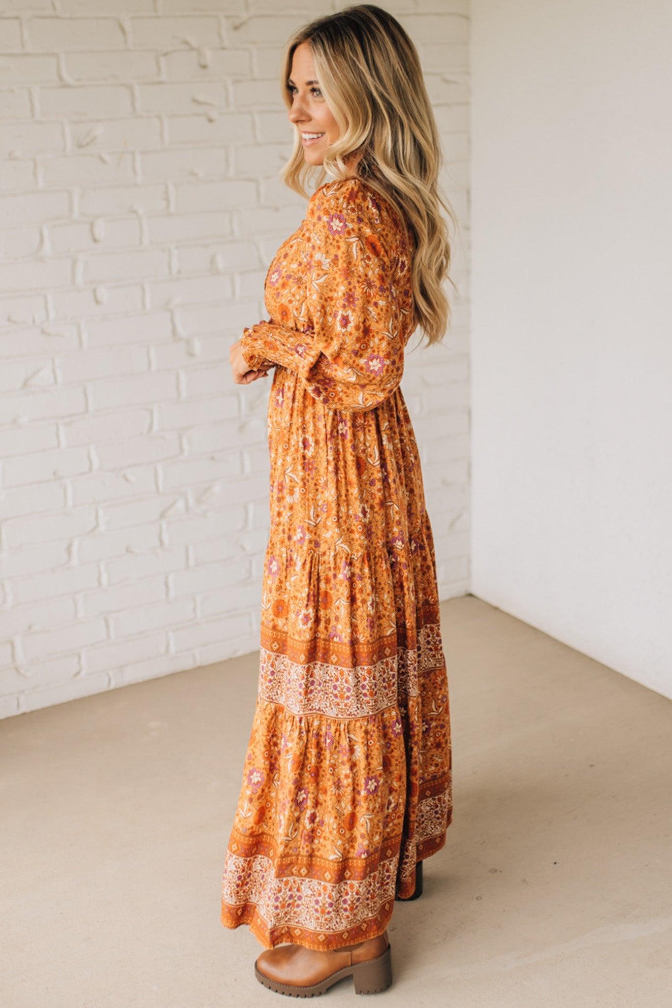Woman wearing an orange floral dress standing against a white brick wall.