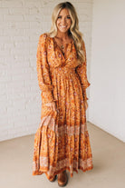 Woman wearing a long orange floral dress against a white brick wall.