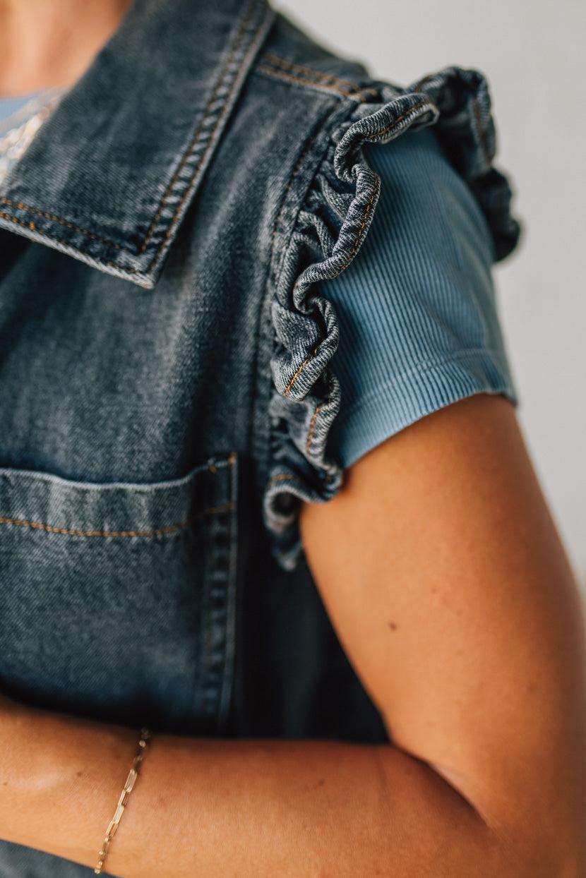 Person wearing a denim vest over a light blue shirt with a neutral background