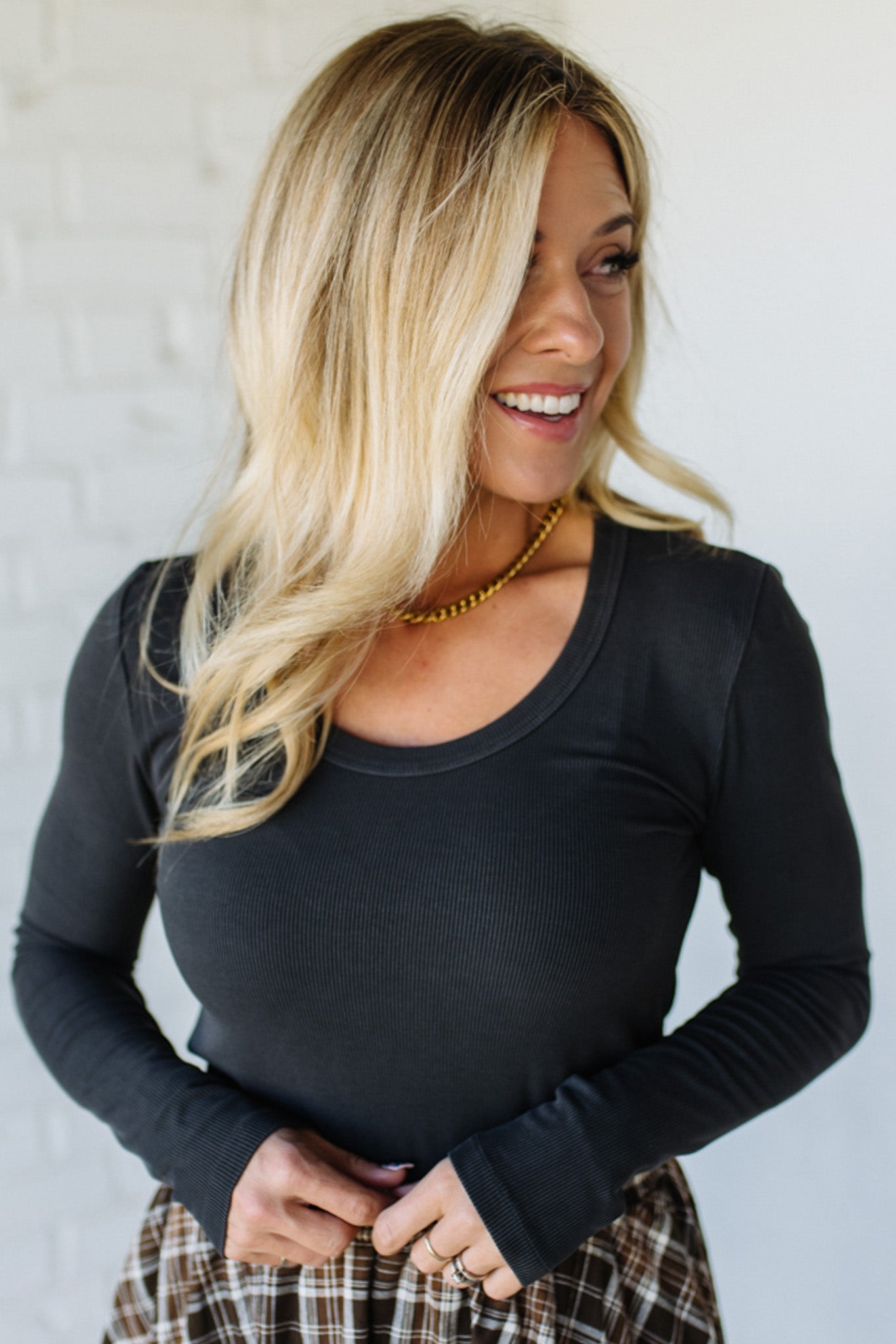 Woman wearing a charcoal long-sleeve top and plaid skirt against a white background