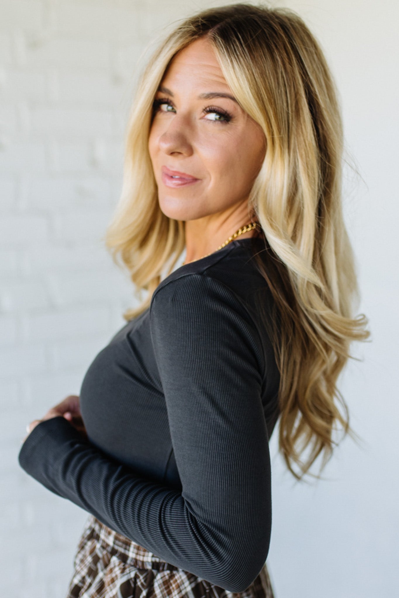 Woman with long blonde hair wearing a charcoal top against a light background