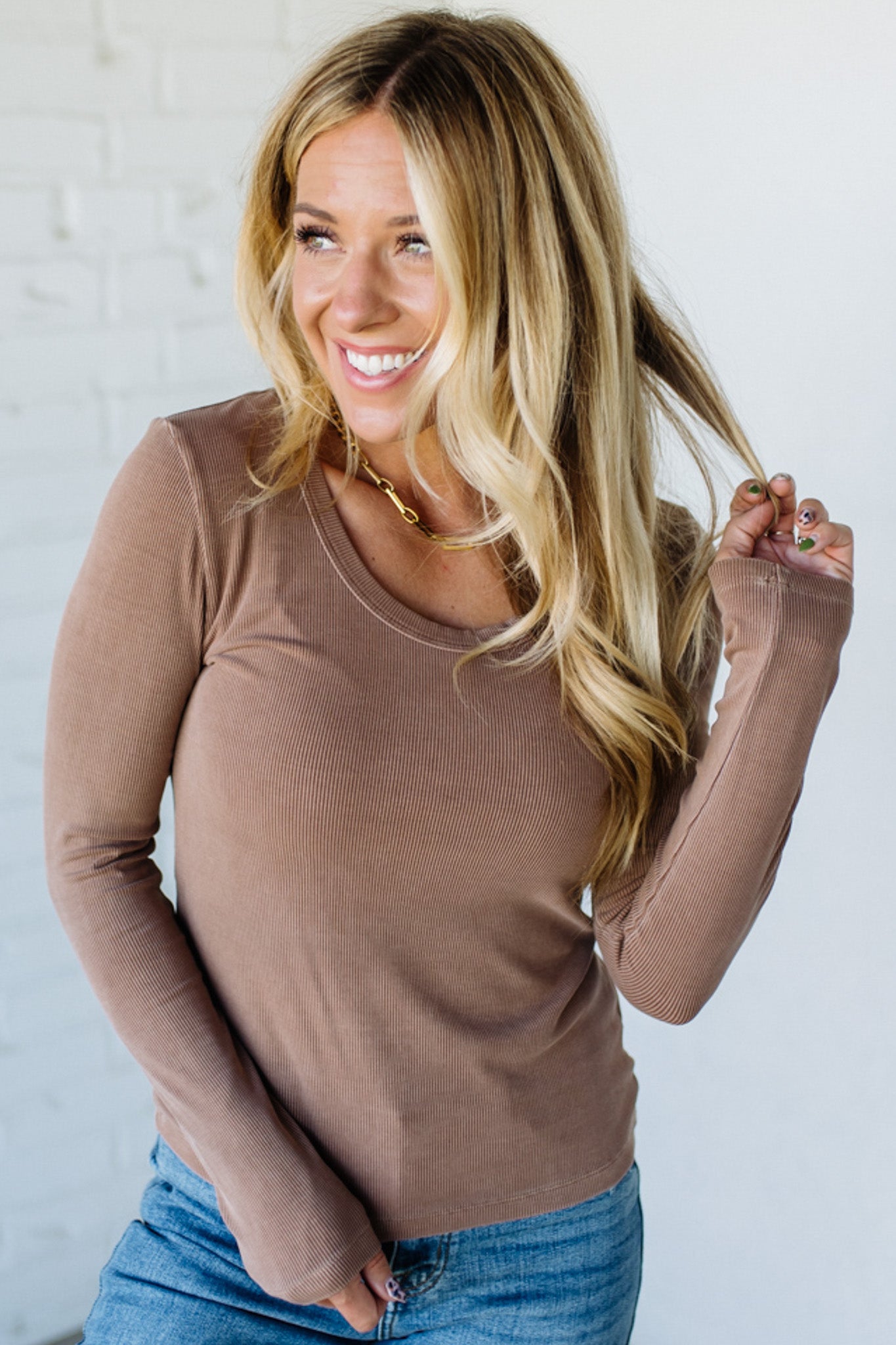 Woman wearing a brown long-sleeve top and blue jeans against a white background