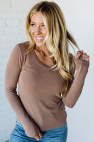 Woman wearing a brown long-sleeve top and blue jeans against a white background