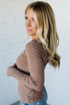 Woman wearing a brown ribbed long-sleeve top against a light background