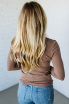 Person wearing a brown long-sleeve top and blue jeans against a white wall.