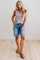 Woman wearing a striped tank top and denim shorts standing against a white wall.