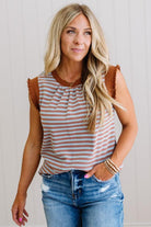 Woman wearing a striped tank top with brown shoulder pads and blue jeans against a neutral background