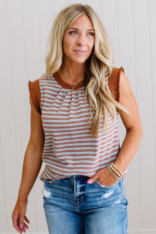 Woman wearing a striped tank top with brown shoulder pads and blue jeans against a neutral background