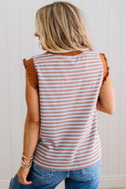 Woman wearing a striped sleeveless top with ruffled shoulders against a white wall.