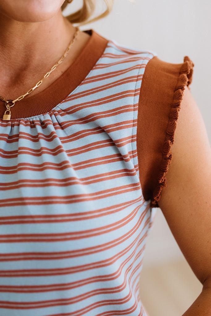 Close-up of a person wearing a striped shirt with brown sleeves and a gold necklace.