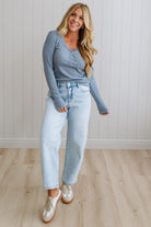 Woman wearing a blue top and light blue jeans standing against a white paneled wall.