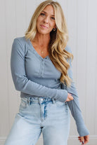 Woman wearing a blue long-sleeve top and light blue jeans against a white wall.