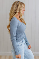 Woman wearing a blue long-sleeve top and light blue jeans against a white wall.