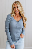 Woman wearing a blue long-sleeve top and light blue jeans against a white wall.