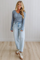 Woman wearing a blue long-sleeve top and light blue jeans standing against a white paneled wall.