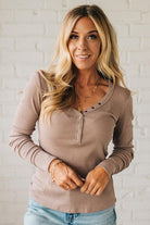 Woman wearing a brown long-sleeve top with buttons against a white brick wall.
