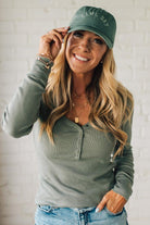 Woman wearing a green cap and matching long-sleeve shirt with a white background