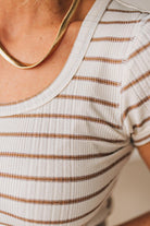 Blonde woman wearing a scoop neck, slim fit tee with vertical ribbed pattern, and horizontal printed stripes.