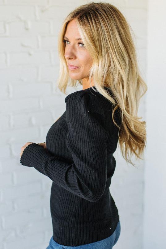 Woman wearing a black sweater against a white brick wall