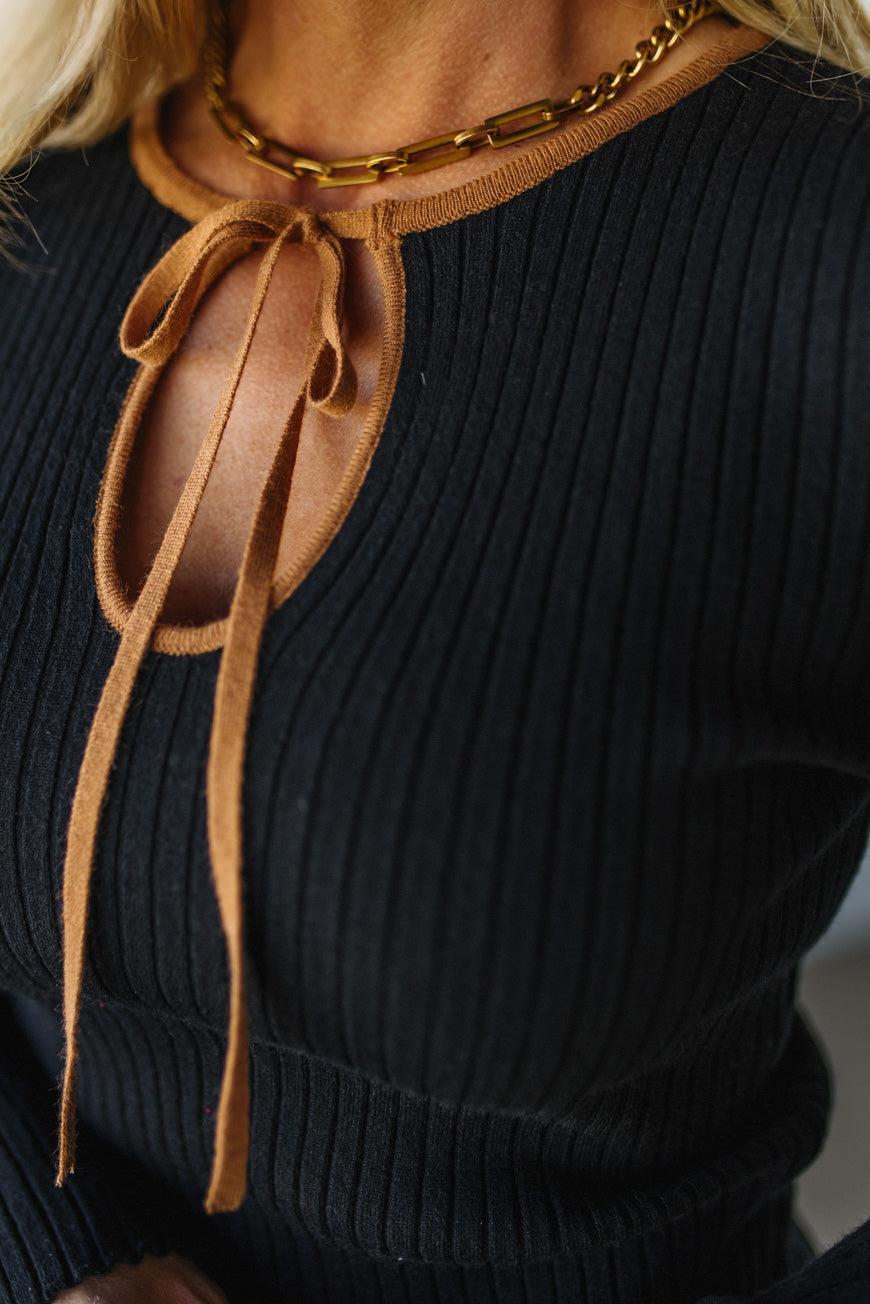 Black ribbed sweater with a brown leather tie detail on a blurred background