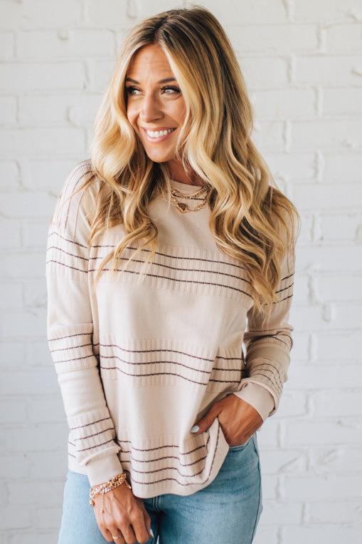 Woman wearing a striped sweater and jeans against a white brick wall
