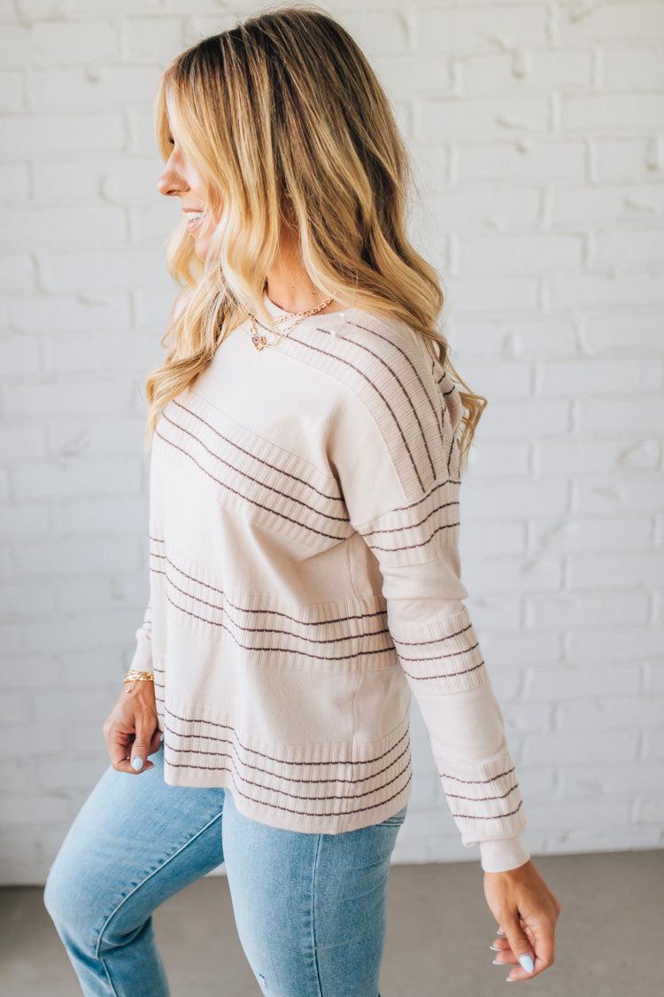 Woman wearing a cream-colored long-sleeve top with mocha stripes against a white brick wall.
