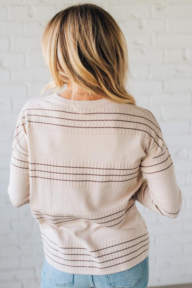 Person wearing a beige sweater with black stripes against a white brick wall