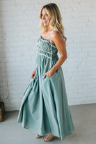 Woman wearing a light green dress with white straps against a white brick wall.