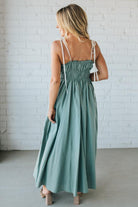 Woman wearing a green dress with white straps against a white brick wall.