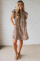 Blonde woman wearing an all over leopard print loose dress with side pockets, and layered ruffle sleeves trimmed with rickrack.