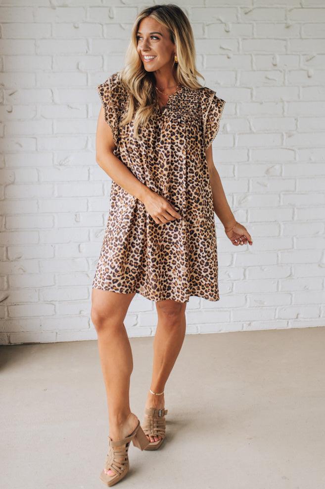Blonde woman wearing an all over leopard print loose dress with side pockets, and layered ruffle sleeves trimmed with rickrack.