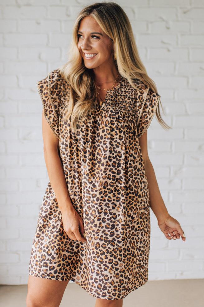 Blonde woman wearing an all over leopard print loose dress with side pockets, and layered ruffle sleeves trimmed with rickrack.