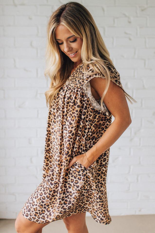 Blonde woman wearing an all over leopard print loose dress with side pockets, and layered ruffle sleeves trimmed with rickrack.