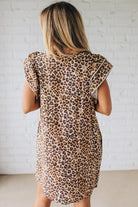 Blonde woman wearing an all over leopard print loose dress with side pockets, and layered ruffle sleeves trimmed with rickrack.