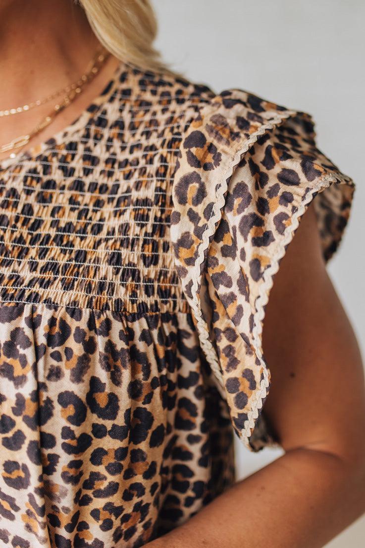 Blonde woman wearing an all over leopard print loose dress with side pockets, and layered ruffle sleeves trimmed with rickrack.