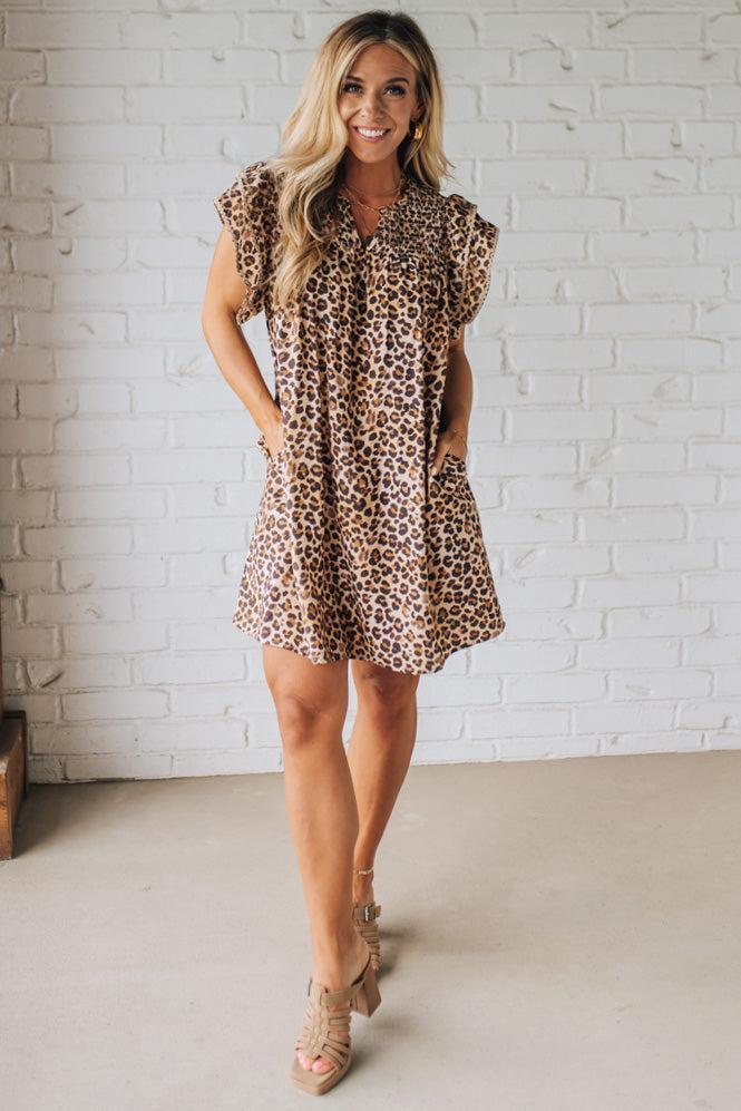 Blonde woman wearing an all over leopard print loose dress with side pockets, and layered ruffle sleeves trimmed with rickrack.