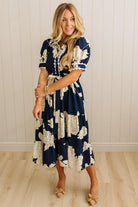 Woman wearing a navy floral dress standing against a white paneled wall.