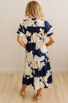 Woman wearing a navy and white floral dress against a light wooden floor and wall.