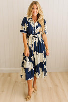 Woman wearing a navy floral dress standing against a white paneled wall.