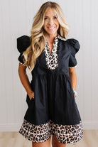 BLONDE WOMAN IN A BRIGHTLY LIT STUDIO WITH LIGHT WOOD FLOORS WEARING LIGHT TAN COWBOY BOOTS AND A BLACK KNEE LENGTH DRESS WITH LEOPARD PRINT ACCENT AND RICKRACK DETAILING.